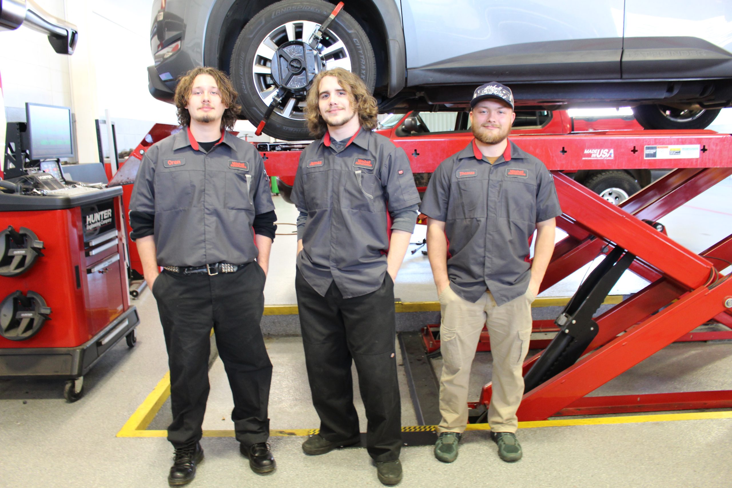 Three Geneva County Automotive Tech students stand together wearing their custom Mitchell Nissan technician shirts.